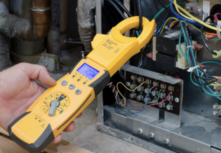 HVAC technician checking thermostat wiring with a digital multimeter during system installation.